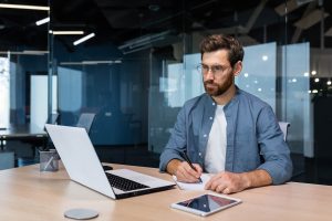 serious businessman is writing down information studying online while sitting inside the office